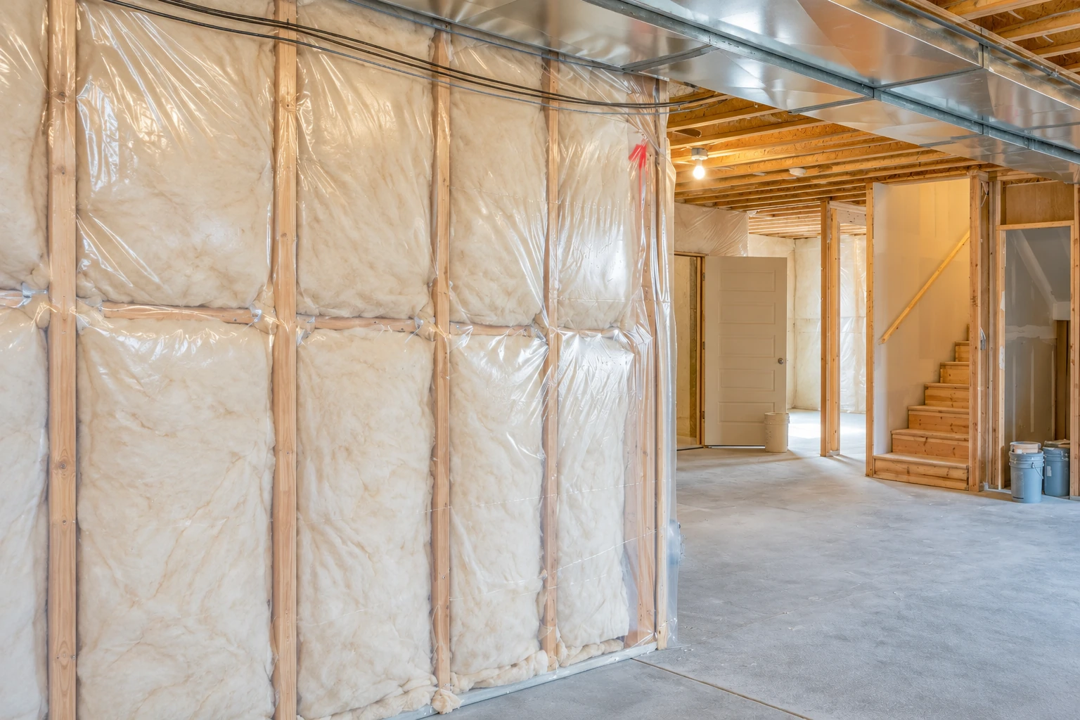Fiberglass batts fill the framed walls of an unfinished basement beneath exposed ductwork.