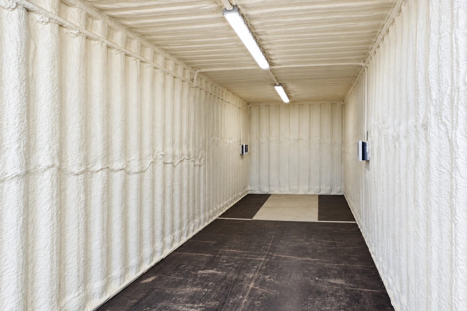 White spray foam coats the walls and ceiling of a commercial container interior.