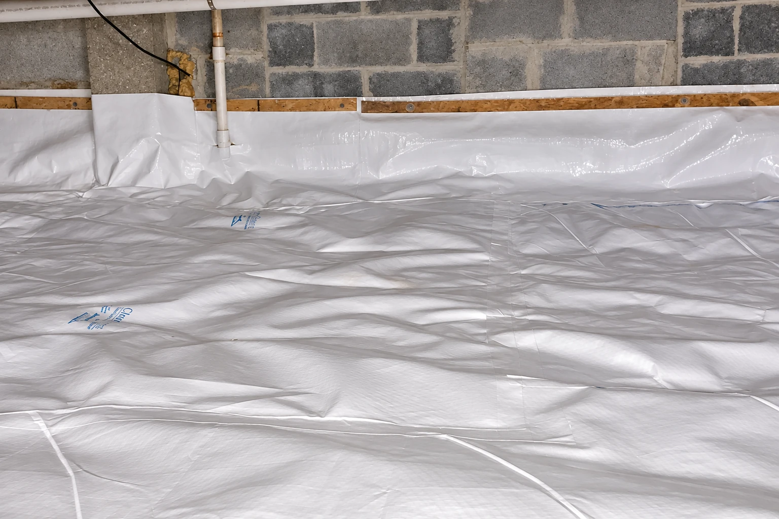 A crawl space floor and lower block walls are covered with wrinkled white vapor barrier sheeting.