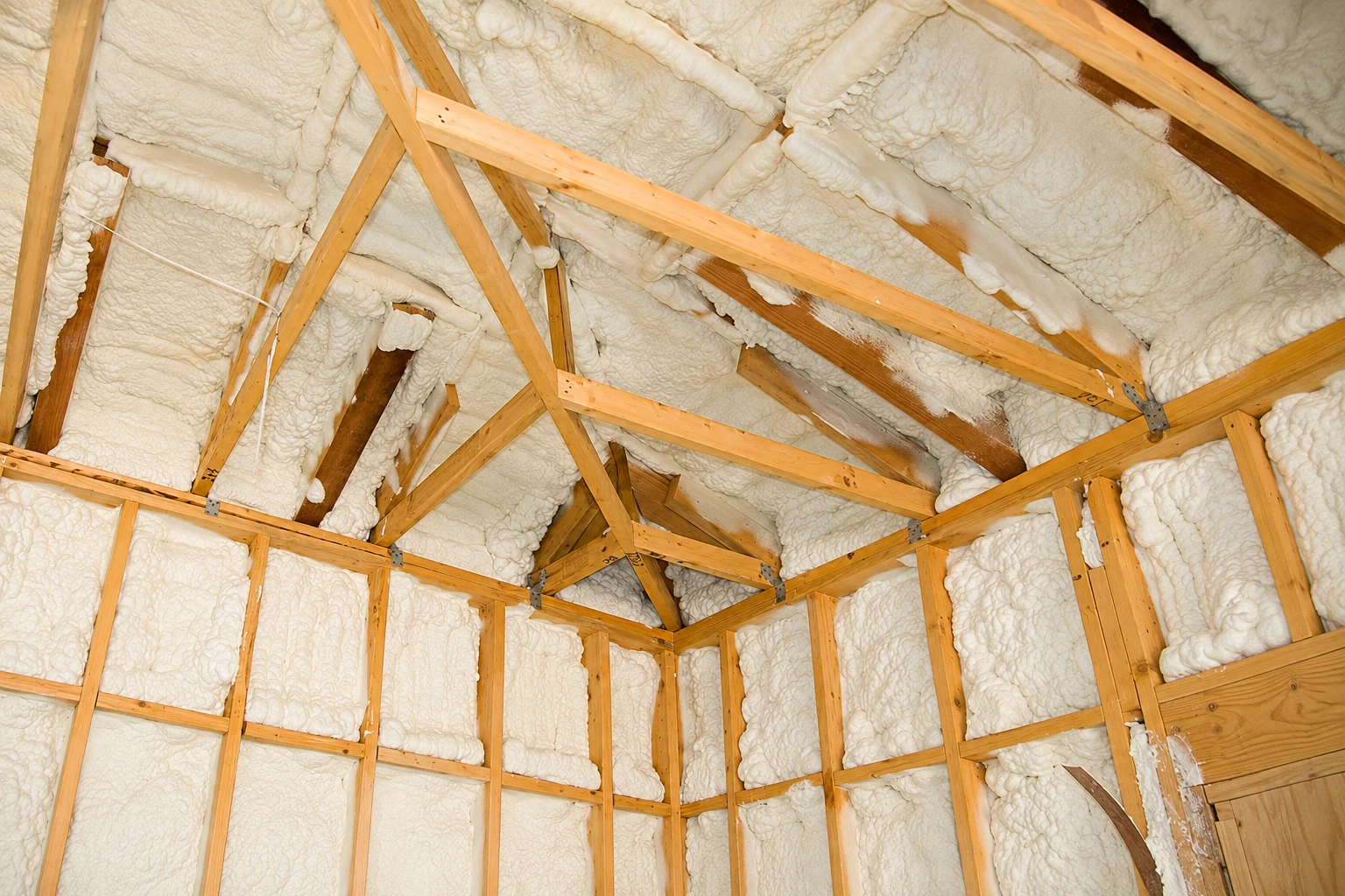 Open-cell spray foam fills the roof and wall cavities between exposed wooden framing in an unfinished attic.